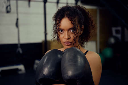 Female boxer training at the gym with boxing gloves on. Mixed race female holding boxing gloves in...