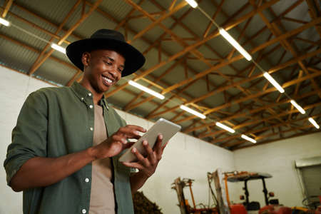 Mixed race male farmer typing on digital tablet standing in farm dairy storeroom . High quality photoの写真素材