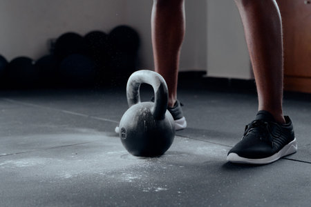 Close-up of young black man wearing sports shoes by chalked kettlebell at the gymの写真素材