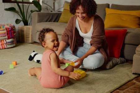 Happy biracial mother playing with daughter in casual clothing in living room at homeの写真素材