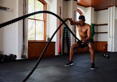 Determined young black man doing a workout with battle ropes at the gym