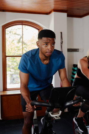 Young black man and caucasian woman in sportswear doing cardio on exercise bike at the gymの写真素材