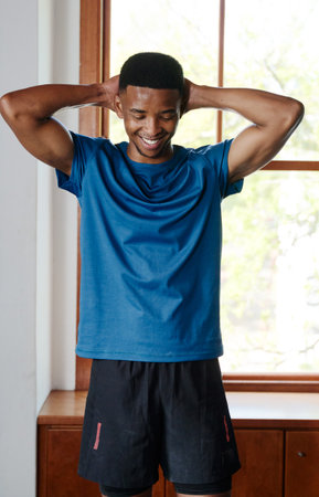 Confident smiling young black man in sportswear with hands behind head at the gymの写真素材
