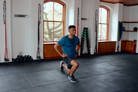 Determined young black man in sportswear doing lunges with hands on hips at the gym