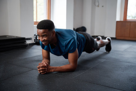 Happy young black man in sportswear doing plank exercises with hands clasped at the gymの写真素材