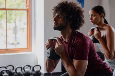 Young middle eastern man and biracial woman in sportswear doing kettlebell squats at the gym