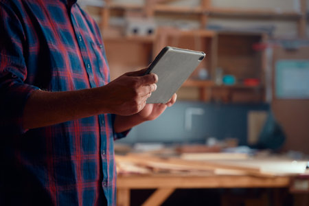 Close-up of multiracial mid adult man in checked shirt using digital tablet at woodworking factoryの写真素材