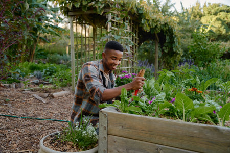 Young black man wearing checked shirt smiling while using spade in flowerbed in garden center