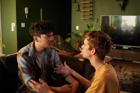 Young gay couple wearing casual clothing face to face while arguing and gesturing in living room at...