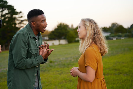 Angry young multiracial couple face to face shouting and gesturing in fieldの写真素材