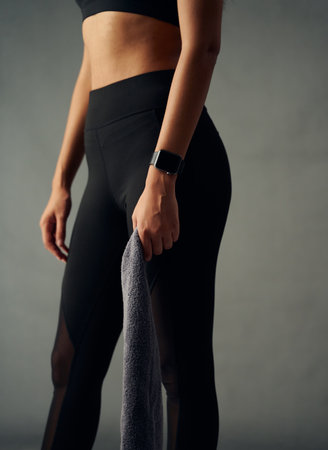 Close-up of fit biracial young woman wearing fitness tracker and leggings holding towel in studioの写真素材