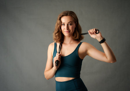Portrait of healthy young caucasian woman in sports clothing holding skipping rope in studio