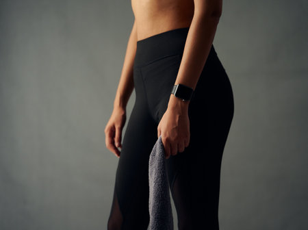 Close-up of fit biracial young woman with fitness tracker wearing leggings and holding towel in studioの写真素材
