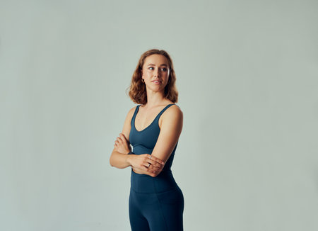 Young caucasian woman wearing sportswear looking over shoulder with arms crossed in studioの写真素材