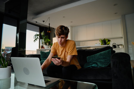 Young caucasian man in casual clothing holding credit card while doing online shopping on laptop at homeの写真素材