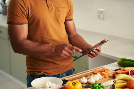 Close-up of young biracial man wearing casual clothing using digital tablet next to food in kitchenの写真素材