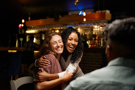 Happy young multiracial group of friends wearing casual clothing hugging at restaurantの写真素材