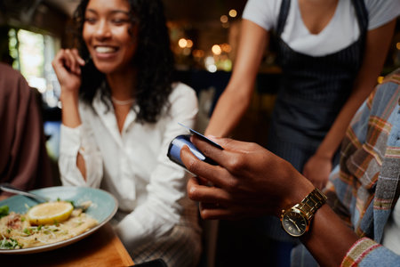 Close-up of happy multiracial friends wearing casual clothing paying waitress for dinner at restaurantの写真素材