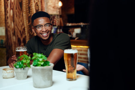 Happy young multiracial friends wearing casual clothing smiling and gesturing with drinks at restaurantの写真素材