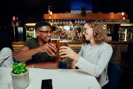 Happy young multiracial group of friends wearing casual clothing smiling while toasting with drinksの写真素材