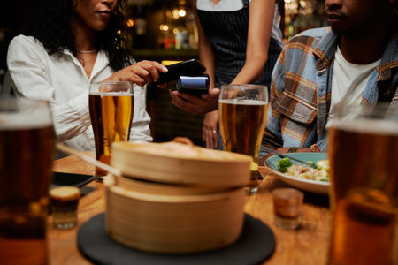 Young multiracial group of friends wearing casual clothing paying waitress for dinner and drinks at barの写真素材