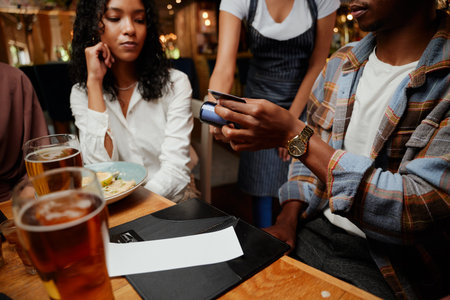 Close-up of multiracial friends wearing casual clothing paying waitress for dinner and drinks bill at barの写真素材