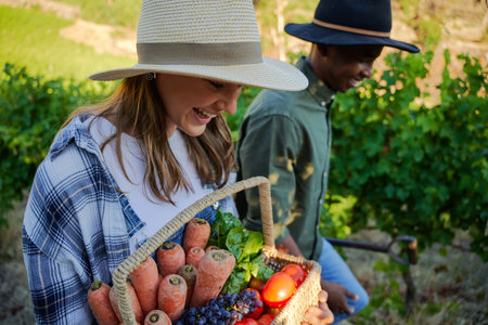 Happy young multiracial couple wearing casual clothing smiling with basket of fresh vegetables on farmの写真素材