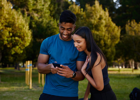Young multiracial couple wearing sportswear smiling while using mobile phone in parkの写真素材