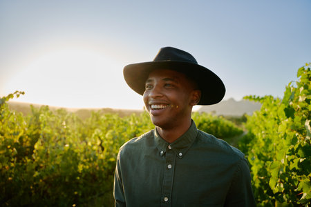 Portrait of happy young black man wearing brimmed hat smiling next to crops on farm
