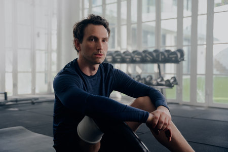 Young caucasian man wearing sportswear with prosthetic leg sitting and taking a break at the gymの写真素材