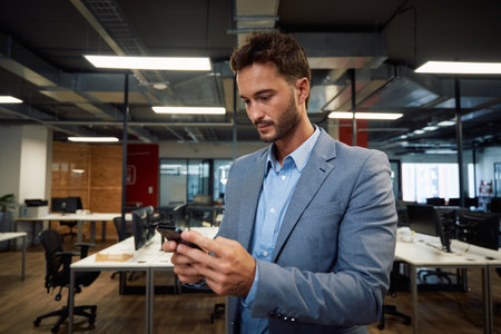 Focused young caucasian man in businesswear using mobile phone in corporate office