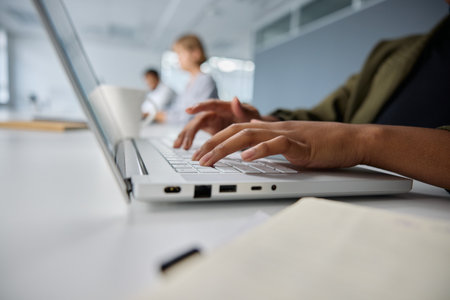 Close-up of three young multiracial business people wearing businesswear typing on laptop at desk in...