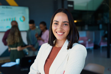 Portrait of smiling young businesswoman in modern office with colleagues in background
