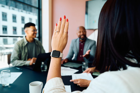 Young businesswoman raising hand to ask question during meeting in modern boardroom at office during...