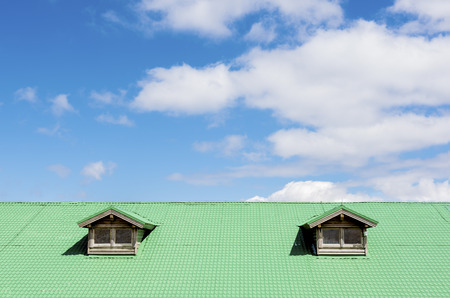 Green roof with two windows against blue sky and cloudsの写真素材