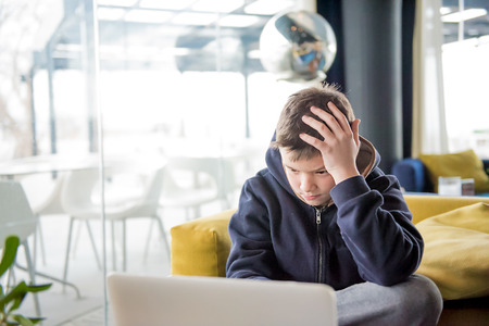 Boy with the  hand on his head is sitting and playing with a tablet computer deviceの写真素材