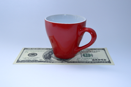 A red cup of coffee is on a 100 dollar billの写真素材
