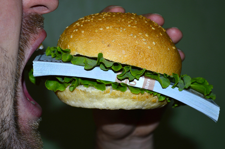 A burger with a batch of dollars bites a manの写真素材