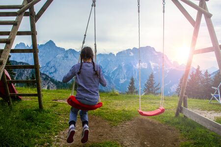 A girl rides on a swing on a background of alpine mountains close up