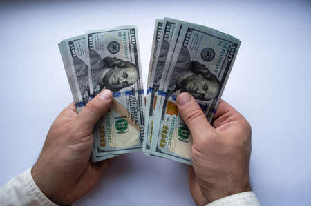 The man's hands are counting one hundred dollar bills close up