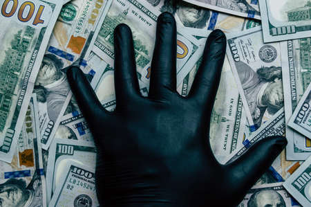 A hand in a black glove holds dollar bills close upの写真素材