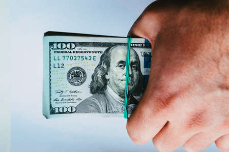 Hand holds dollar banknotes rewound with rubber band close upの写真素材