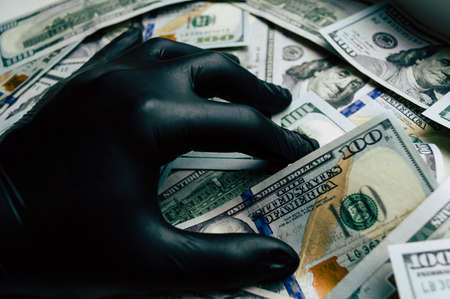 A hand in a black glove holds dollar bills close up