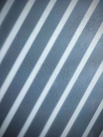 Blinds shade on a light textured wall close up.