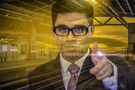 Young businessman Wear glasses square, Finger pointing forward On sky train station with sunshine, Background yellow evening sky, With concept of abstract  Up-Down and Ready-to-Run Businessの写真素材