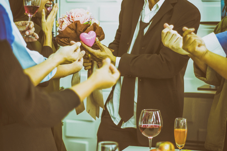 Girl smiled excitedly as businessman gave flowers and a heart-shaped symbol, Among group of friends at party congratulated mini heart, With vintage color schemeの写真素材
