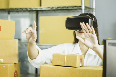 Asian women start up small business owner,hand using vr to communicate,with cardboard box for packing products,in at home office,online sales concept and e-commerce and product delivery business.の写真素材