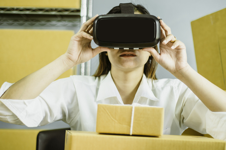 Asian women start up small business owner, are using vr to communicate , with cardboard box for packing products, in at home office, online sales concept and e-commerce and product delivery business.の写真素材