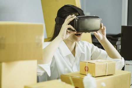 Asian women start up small business owner, are using vr to communicate , with cardboard box for packing products, in at home office, online sales concept and e-commerce and product delivery business.の写真素材