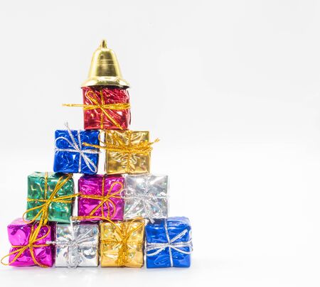 There are gift boxes in various colors, including red, gold, silver, blue, and green, arranged in layers like a Christmas tree and on the top there are bells.の写真素材